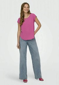 Top rosa de mangas curtas combinado com jeans de cintura alta e pernas largas em azul claro. Modelo usa sandálias de salto alto rosa. Decote e corte simples.