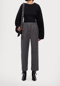 Haut à manches longues noir, pantalon taille haute gris, sac à main noir avec des accents métalliques, et bottines noires à lacets.