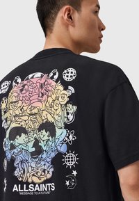 T-shirt en coton noir avec un imprimé graphique coloré de personnages et de symboles divers au dos, avec la marque "ALLSAINTS" en bas.