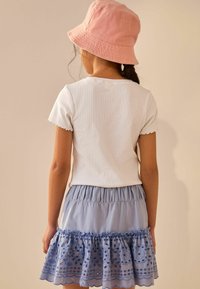 Chemisier blanc à rayures avec des bords festonnés, associé à une jupe à volants bleu clair comportant des motifs brodés et un ourlet à volants. Chapeau seau rose.