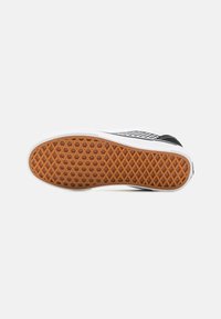 Sole di sneaker in bianco e nero con una presa in gomma marrone texturizzata, caratterizzata da un motivo a diamante e accenti laterali bianchi.