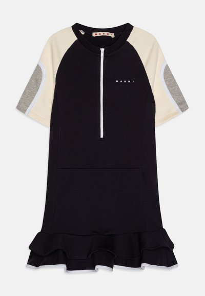 Crna haljina s kratkim raglan rukavima, kremastim i sivim detaljima, prednjim patentnim zatvaračem i volanima na rubu. Materijal izgleda mekano i rastezljivo.