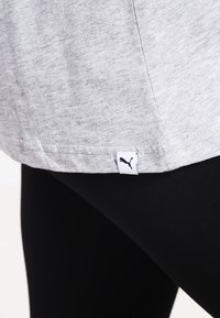 Jasnoszara koszulka wykonana z miękkiej tkaniny, z zaokrąglonym dołem. Na dole po lewej stronie znajduje się mała czarna metka z logo Puma.