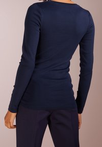 Marinblå långärmad topp av mjukt material, med rund halsringning och figursydd passform, synliga sömmar längs kanterna.