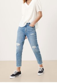 Light blue ripped jeans with a relaxed fit, featuring distressed details and a high waist. Paired with a white textured blouse and black sneakers.