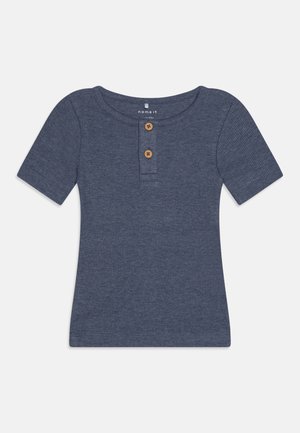 Tamno plava majica s kratkim rukavima od rebraste tkanine s okruglim izrezom, koja ima dva drvena dugmadi na prednjem dijelu.