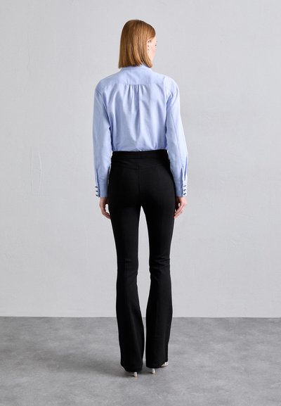 Light blue button-up shirt with tailored back pleats, paired with high-waisted black flared pants. Features include button accents on sleeve.