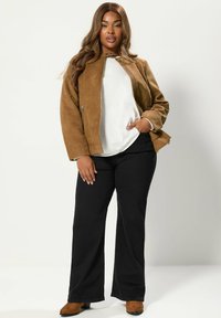 Brun mockaskinnjacka med en figurnära design, vit topp och svarta utsvängda byxor. Modellen bär brun ankelboots. Släta texturer och mjuka färger.