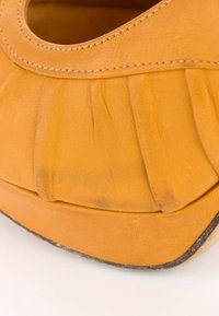 Gros plan de la zone des orteils d'une chaussure en cuir jaune usée avec des plis visibles et des marques d'usure sur les bords de la semelle.