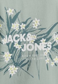 Lichtgroene katoenen t-shirt met een bloemenontwerp met witte bloemen en groene bladeren. De merknaam "JACK & JONES" is gedrukt in vetgedrukte witte tekst.