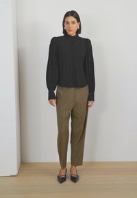 Blusa nera a maniche lunghe in riga con colletto alto abbinata a pantaloni a righe verde oliva. A completare l'outfit, delle ballerine nere a punta.