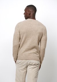 Suéter de punto beige con cuello y puños acanalados, que presenta un acabado texturizado. Lleva puesto un pantalón de pana beige claro.