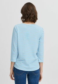 Top a maniche lunghe blu e bianche a righe con scollatura rotonda e orlo leggermente curvo. Il tessuto presenta un motivo testurizzato di pois.
