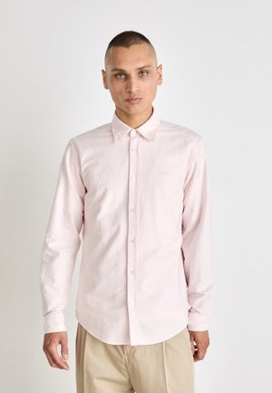 Light pink long-sleeve shirt with white vertical stripes, button-down collar, and curved hem. Features white buttons and a minimal logo.