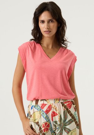 Camiseta de manga corta con escote en V en tela color coral rosa. Combinada con pantalones claros de estampado con motivos tropicales y colores vibrantes.