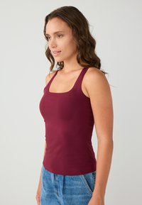 Bordeaux tanktop met een vierkante halslijn, gemaakt van gladde stof, met brede bandjes en een getailleerd ontwerp. Gecombineerd met denim shorts.