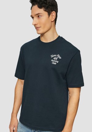 T-shirt en coton bleu marine avec un col rond et des manches courtes. Présente un texte brodé blanc "Club de Course à un Rythme Lent" sur la poitrine gauche.
