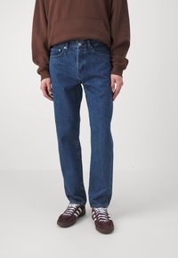 Blå denimjeans med rett bendesign, med knapp og glidelås, frontlommer og slitt tekstur. Sammen med burgunder sneakers.