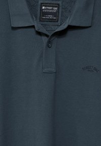 Mörkgrå polo skjorta i texturerad bomull, med knäppning fram, korta ärmar och en subtil präglad logotyp på bröstet.