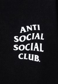Czarna tkanina z napisem "ANTI SOCIAL SOCIAL CLUB" w dużej, stylizowanej białej czcionce, wyśrodkowanym i wyraźnie wyeksponowanym.