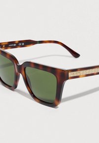 Καφέ γυαλιά ηλίου με σχέδιο καβουριού και πράσινους φακούς. Παχύ τετράγωνο πλαίσιο με διακοσμητικό χρυσό μοτίβο στο μπράτσο. Κατασκευασμένα από πλαστικό.