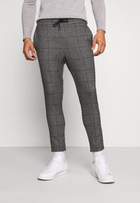 Szare spodnie w kratę wykonane z teksturowanej tkaniny, z elastycznym pasem i sznurkiem, zestawione z białymi sneakersami.