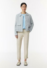 Jasnoniebieska marynarka z tweedu o prostym kroju, okrągłym dekolcie i naszytymi kieszeniami, zestawiona z jasnoniebieską bluzką i kremowymi spodniami w taperze.