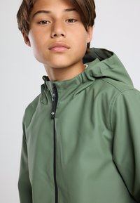 Lightweight green waterproof jacket with a hood, features a front zipper, black accents, and smooth texture.
