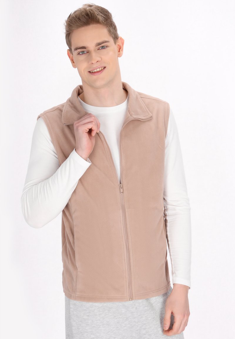 Gilet in pile beige chiaro con zip frontale, collo a camicia e texture liscia. Indossato sopra una maglietta bianca a maniche lunghe.