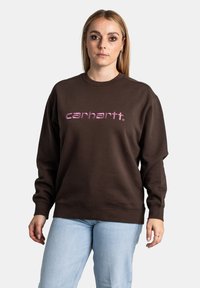 Felpa marrone con scollo rotondo e maniche lunghe. Presenta un logo "carhartt." in rosa stampato sul davanti. Tessuto morbido al tatto.
