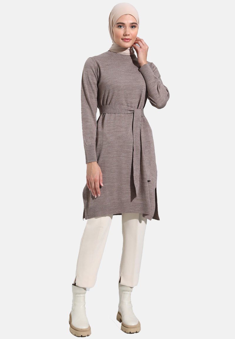 Knit long-sleeve dress in taupe with a belt, featuring side slits. Paired with cream trousers and white ankle boots. Smooth texture.