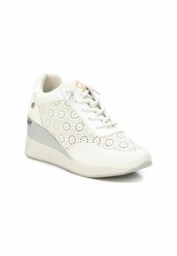 Zapatillas de cuña blancas con un patrón floral perforado, parte superior texturizada, acentos en gris claro, cordones planos y un ligero detalle metálico en el lateral.