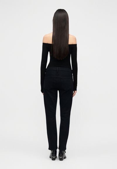 Black off-the-shoulder top paired with fitted black jeans. The model has long straight hair and wears black heeled boots with accents.
