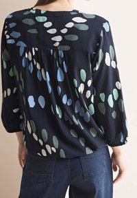 Marinblus med mjuk textur, med ett flerfärgat droppmönster i grönt, ljusblått och vitt. Elastiska ärmslut och detaljerad bakparti.