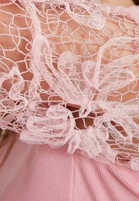 Détail du haut rose avec une dentelle douce et texturée ornée de motifs floraux et un design en filet le long du décolleté et des manches.