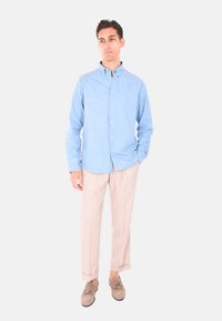 Camicia button-up azzurro chiaro con maniche lunghe, in cotone; abbinata a pantaloni beige e mocassini marroni.