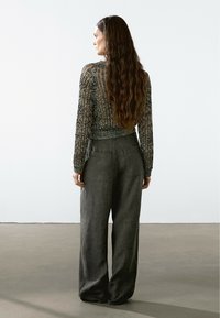 Langärmliger, strukturierter Strickpullover in Schwarz und Grau, kombiniert mit weit geschnittenen, grauen Leinenhosen, von hinten betrachtet.