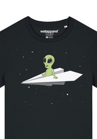 Schwarzes Baumwoll-T-Shirt mit einem Grafikdesign eines grünen Aliens auf einem weißen Papierflieger vor einem sternenbesäten Hintergrund.