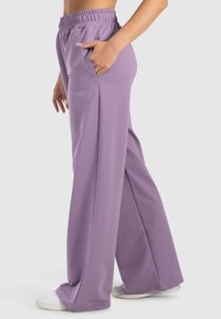 Lila weit geschnittene Hose aus weichem Stoff, mit elastischem Bund, seitlichen Taschen und bestickten Details an der linken Hüfte.