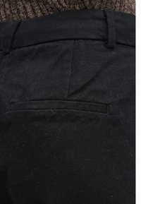 Pantalones negros de tela texturizada, con un único bolsillo trasero con costuras sutiles y un acabado limpio.