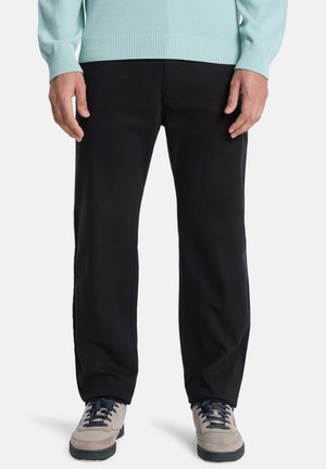 Black trousers, cotton fabric, straight cut, feature pockets, worn with a light blue sweater and gray sneakers with blue accents.