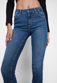 Jeans ajustados de mezclilla azul con una textura suave, cintura alta, bolsillos frontales y un sutil patrón desgastado a lo largo de los muslos.