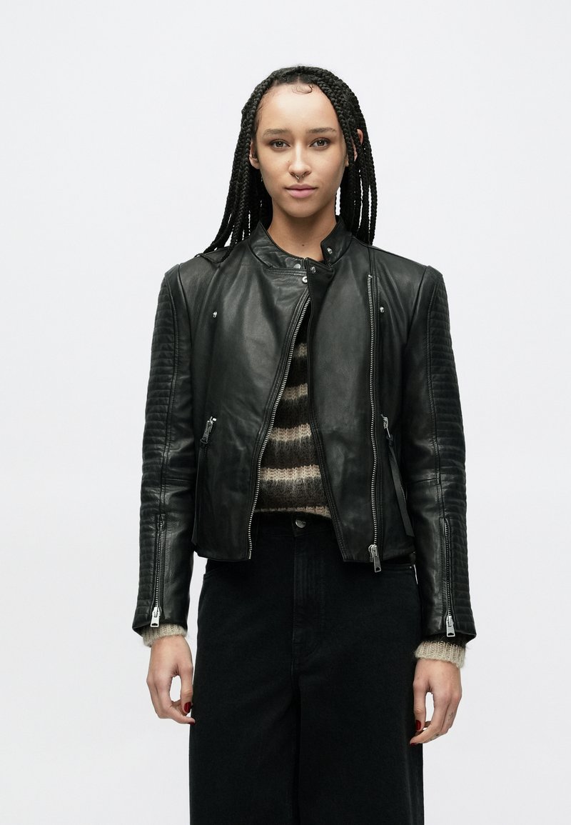 Czarna skórzana kurtka motocyklowa o dopasowanym kroju, z żebrowanymi akcentami na rękawach oraz zamkami błyskawicznymi z przodu i na mankietach.