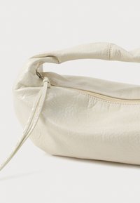 Borsa a mano in pelle bianca con forma arrotondata, finitura testurizzata e manico superiore singolo. Presenta una chiusura con zip e un design minimalista.