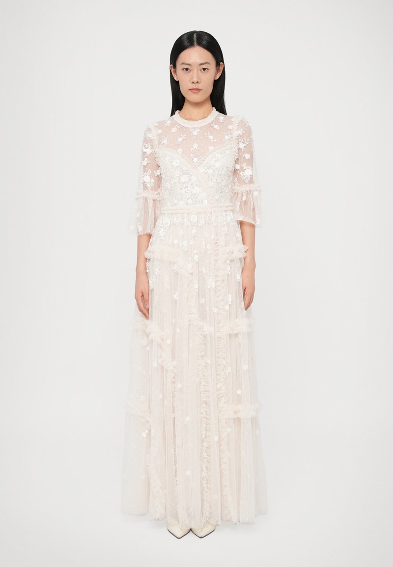 Rochie lungă, ivoirie, cu o suprapunere transparentă din dantelă florală, detalii cu volane și mâneci evazate. Talie mulată care se prelungește într-o fustă fluidă, în straturi.