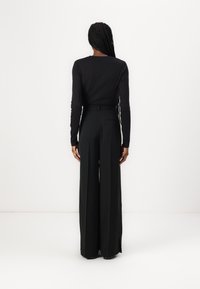 Haut noir à manches longues et pantalon noir taille haute à jambes larges. Tissu lisse avec un minimum de détails et poches arrière dissimulées.