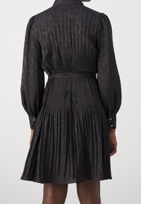 Vestido negro de camiseta con un estampado de leopardo, textura plisada, cintura ajustada y mangas largas con puños de botón.