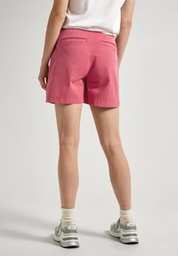 Pantaloni corti di cotone rosa con taglio dritto, caratterizzati da tasche posteriori e orlo pulito. Abbinati a scarpe da ginnastica grigie e calzini bianchi alla caviglia.