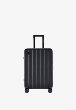 Black hard-shell suitcase featuring vertical grooves, retractable handle, and four spinner wheels for easy mobility.