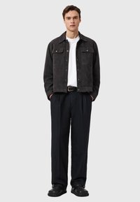 Dark suede jacket with two chest pockets, paired with a white t-shirt, loose black trousers, and black shoes. Simple, modern design.